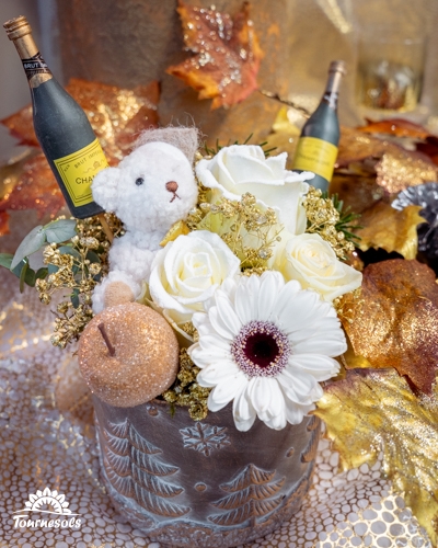 Composition florale Nouvel An blanche et dorée avec roses, gerbera, ourson et mini bouteilles de champagne